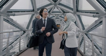 Slow motion of excited businesspeople Asian man and Middle Eastern woman in hijab dancing walking in contemporary glass hallway celebrating success. professional achievement concept.