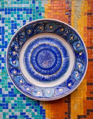 Naklejka premium Blue and white ceramic plate on a background of colorful mosaic tiles.