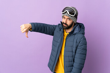 Skier man with snowboarding glasses over isolated purple background showing thumb down with negative expression