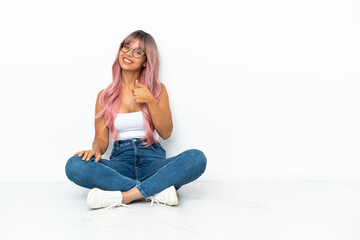 Young mixed race woman with pink hair sitting on the floor isolated on white background giving a...