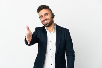 Telemarketer man working with a headset isolated on white background shaking hands for closing a good deal