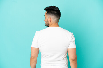 Young caucasian man isolated on blue background in back position and looking side