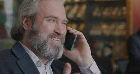 Close-up of joyful businessman speaking on mobile phone laughing discussing successful deal indoors in cafe. Cellphone communication and business concept.
