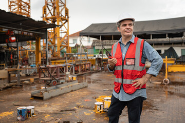 Caucasian mature engineer man worker touching hard hat with crane background