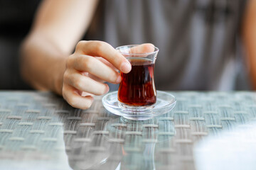 Close-up of man's hand holding glass of Turkish tea on reflection background table
