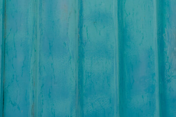 Close-up of a weathered blue metal surface with rust stains and textured patterns. The aged and grungy appearance of the metal creates an industrial backdrop that highlights the contrast between blue 