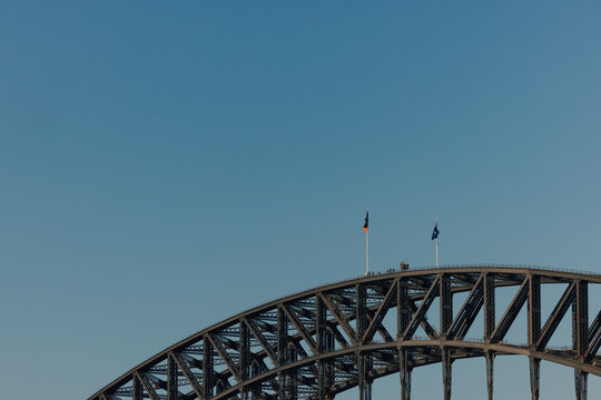 Flags flying at the peak of the Sydney Harbour Bridge with group of people climbing