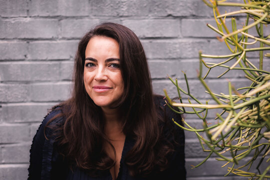 Headshot of a middle aged woman in front of a grey brick wall.