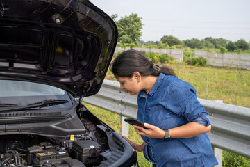 Young Indian woman standing by her car with the hood open, gazing at the damaged engine in frustration as she tries to figure out the problem 