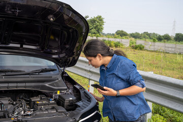 Young Indian woman standing by her car with the hood open, gazing at the damaged engine in frustration as she tries to figure out the problem 