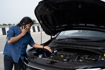 Young Indian woman standing by her car with the hood open, gazing at the damaged engine in frustration as she tries to figure out the problem 