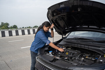 Young Indian woman standing by her car with the hood open, gazing at the damaged engine in frustration as she tries to figure out the problem 
