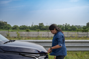 Young Indian woman standing by her car with the hood open, gazing at the damaged engine in frustration as she tries to figure out the problem 