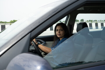 Happy indian woman driving a car in the city. Portrait of smiling female with safety belt traveling in her auto.