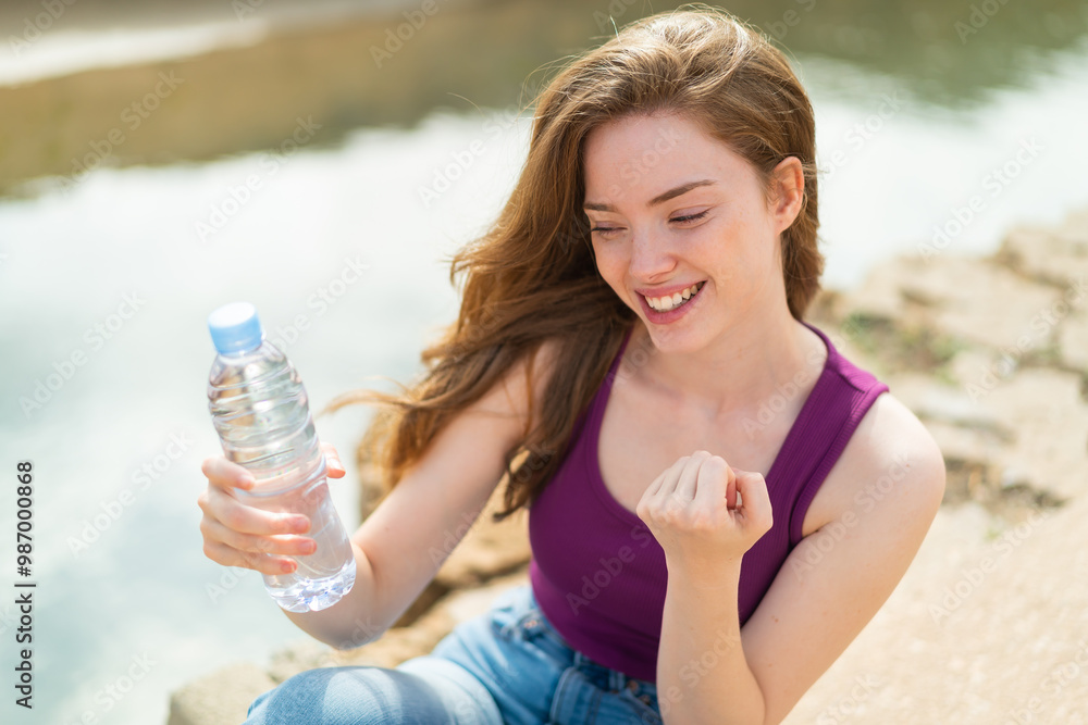 Sticker Young redhead woman with a bottle of water at outdoors celebrating a victory