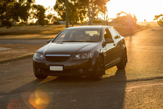 backlit dark coloured car on quiet street in country town with sun flare
