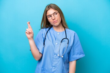 Young surgeon doctor woman isolated on blue background with fingers crossing and wishing the best