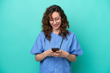 Young nurse caucasian woman isolated on blue background sending a message with the mobile