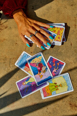 ;A hand with turquoise nails touches scattered tarot cards, symbolizing fortune-telling,...