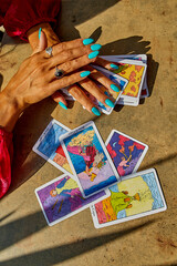Hands with turquoise nails rest on tarot cards, including the King of Cups, Page of Cups, and Five...