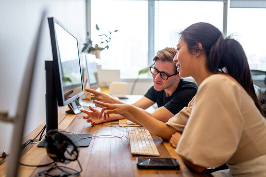 Asian woman pointing to a monitor screen sitting together with a team-mate
