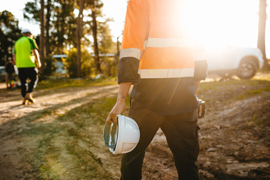 Construction worker holding a helmet and a drill while walking on the construction site.