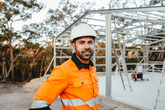 A bearded man standing in front of a metal structure at the construction site.