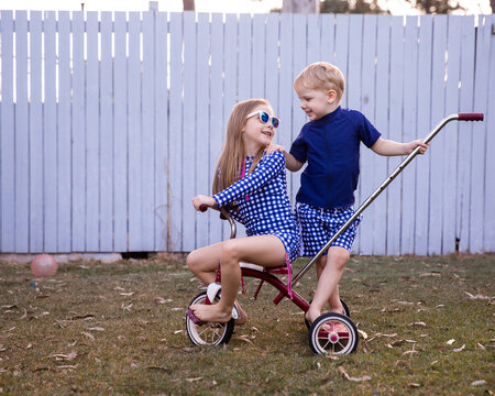 girl on a trike looking at her brother standing on the back