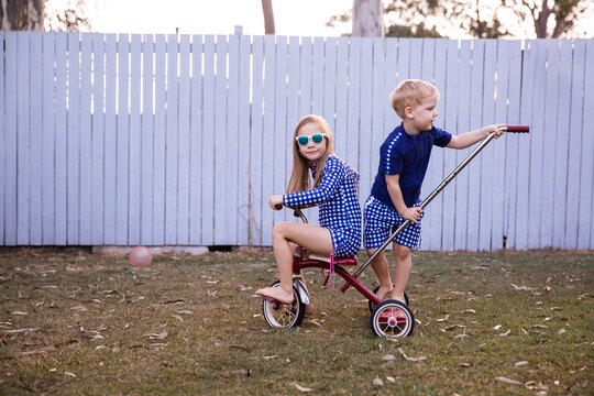 kids riding a trike with a girl in sunnies pedalling and her brother on the back