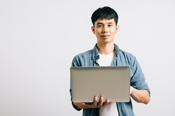 Confident and excited, a young Asian man smiles while working on a laptop, sending emails or chatting online. Studio shot isolated on white background, emphasizing his technological prowess.