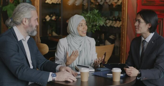 Two businessmen discussing deal while interpreter Muslim woman in hijab translating negotiation during meeting in cafe. Talks and business concept.