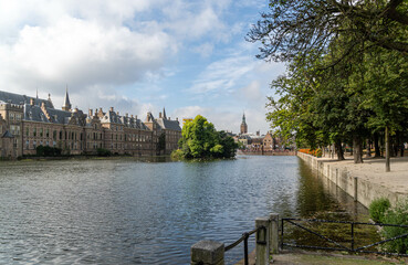  serene water body adjacent to historic buildings and a tree-lined park. The architecture is traditional European, likely a cityscape, calm water reflects the sky and trees