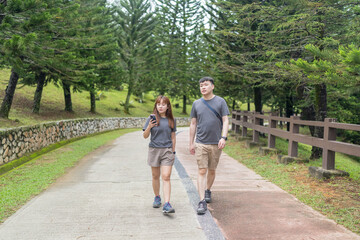 Chinese Malaysian couple in their 30s walking closely together in a lush, water-filled park in Kuala Lumpur, Malaysia.