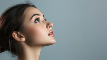 Naklejka premium Close-up portrait of young woman gazing upward against grey background