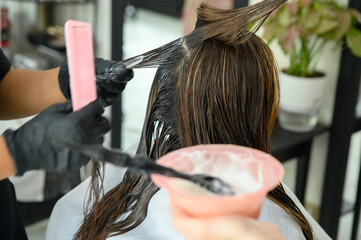 A hairdresser is applying keratin hair straightening solution to the hair of a female customer in a...