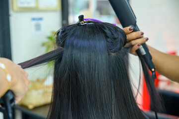 Two hairdressers using hair straighteners Straightening the hair of a female customer to make it beautifully straight in a beauty salon, hair care in Thailand