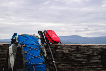 A hiker's backpack and trekking poles rest against a rustic log, with a first aid kit visible. The...