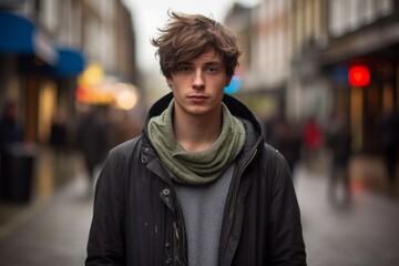 Fototapeta premium A young man wearing a black jacket and scarf stands in the rain