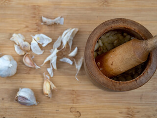 wooden mortar with garlic and a pestle and peeledd garlic aside