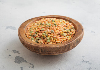 Wooden bowl of dry raw green and orange peas seeds on light table.Macro.