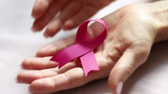 Female hands holding a pink ribbon, closeup