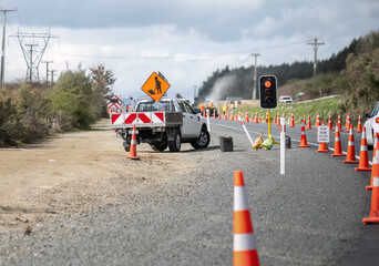Orange traffic cones on the road. Cars stopped at the roadwork red light. Unrecognizable workers on...