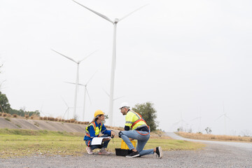 Male and female engineer at windmill field farm, wearing safety uniform and working and inspecting quality of wind turbines