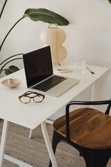 Minimalist Home Office with Laptop, Glasses, and Lamp on White Desk Surrounded by Green Plants....