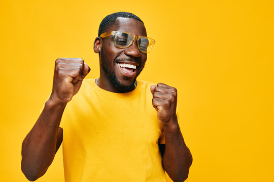Happy man celebrating joyfully in a bright yellow shirt and sunglasses against a vivid yellow background, expressing excitement and positivity, ideal for lifestyle and happiness themes