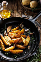 Roasted potato wedges seasoned with rosemary, garlic and olive oil in a cast iron pan, close up view