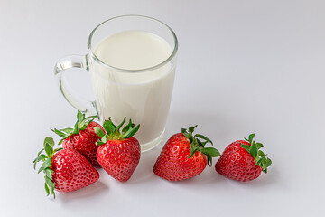 glass mug of milk and sweet fragrant strawberries on a white surface