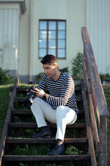 Obraz premium A young male photographer is sitting in front of a house, looking at the camera.