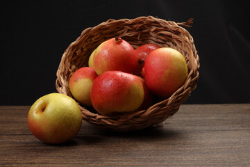 Green yellow red ripe mini pear sweet juicy in basket on wooden table dark background