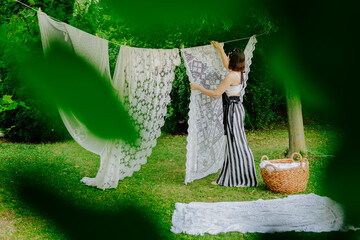 Woman standing in a serene outdoor setting hanging vintage lace fabric on a clothesline.